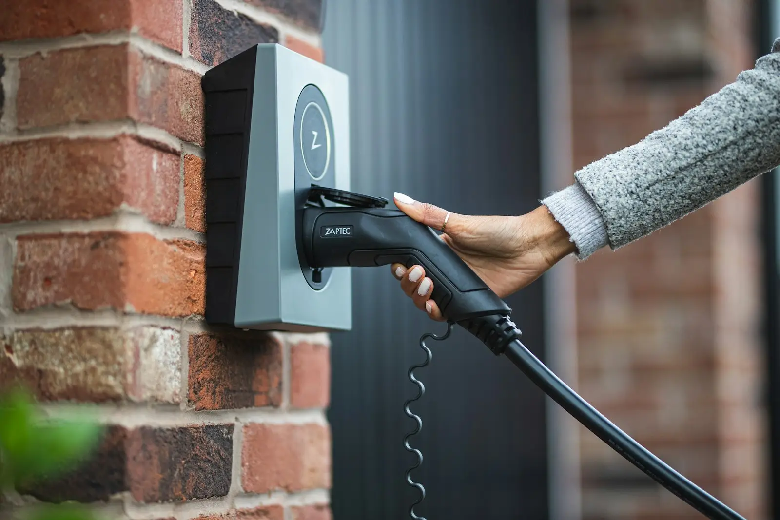 A person plugging an electric car into a wall-mounted charger on a brick wall