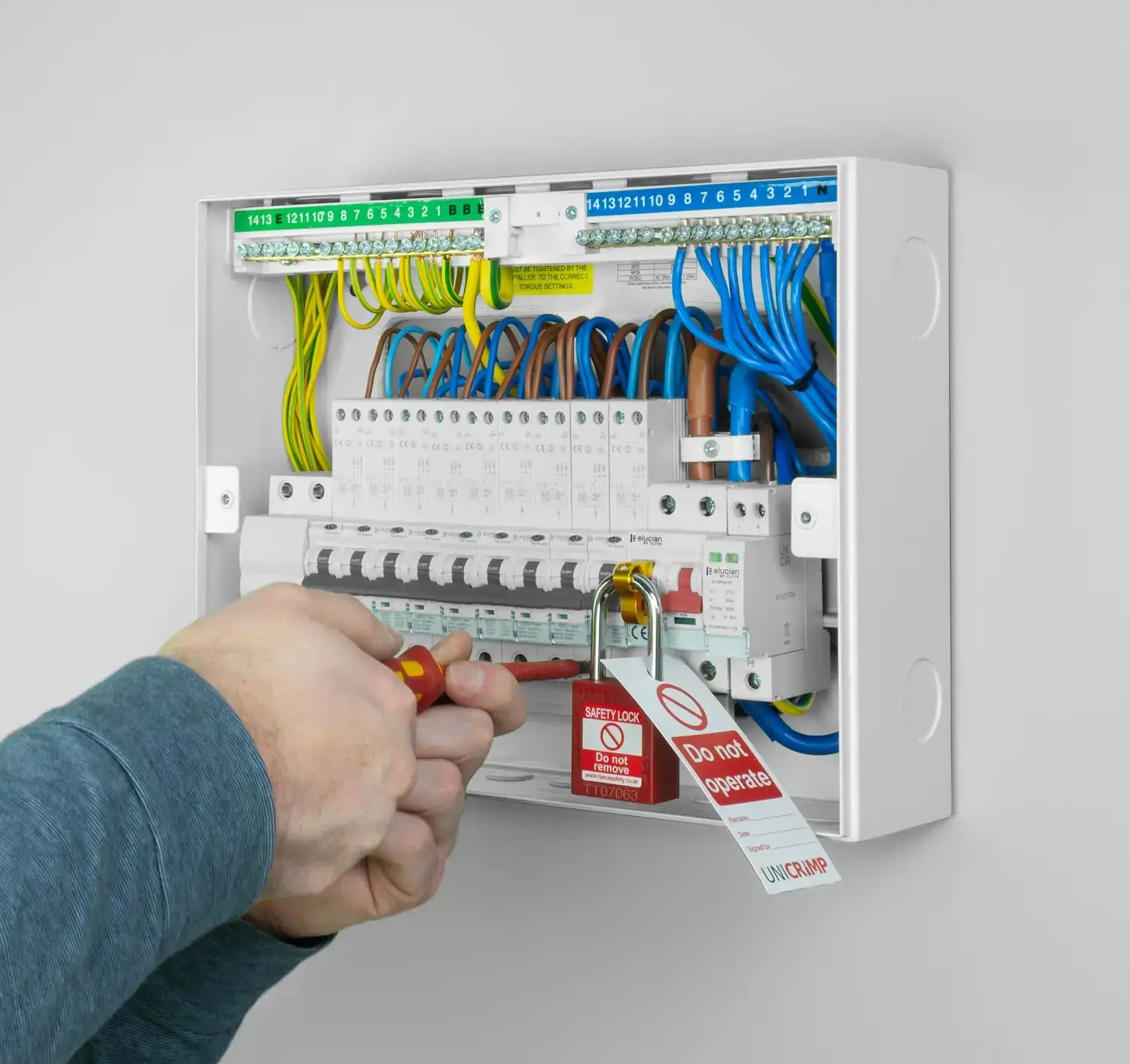 The new consumer unit with its cover off, an electrician locking off a breaker with a safety lock and tag